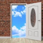 Brick wall with open door in the center, leading to blue sky with clouds.