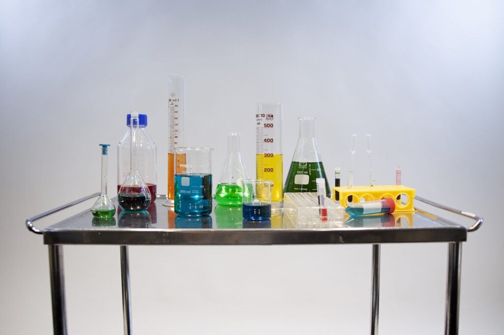 Lab table with a variety of different shapes and sizes of beakers and containers with different colored liquids.