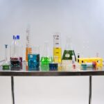 Lab table with a variety of different shapes and sizes of beakers and containers with different colored liquids.
