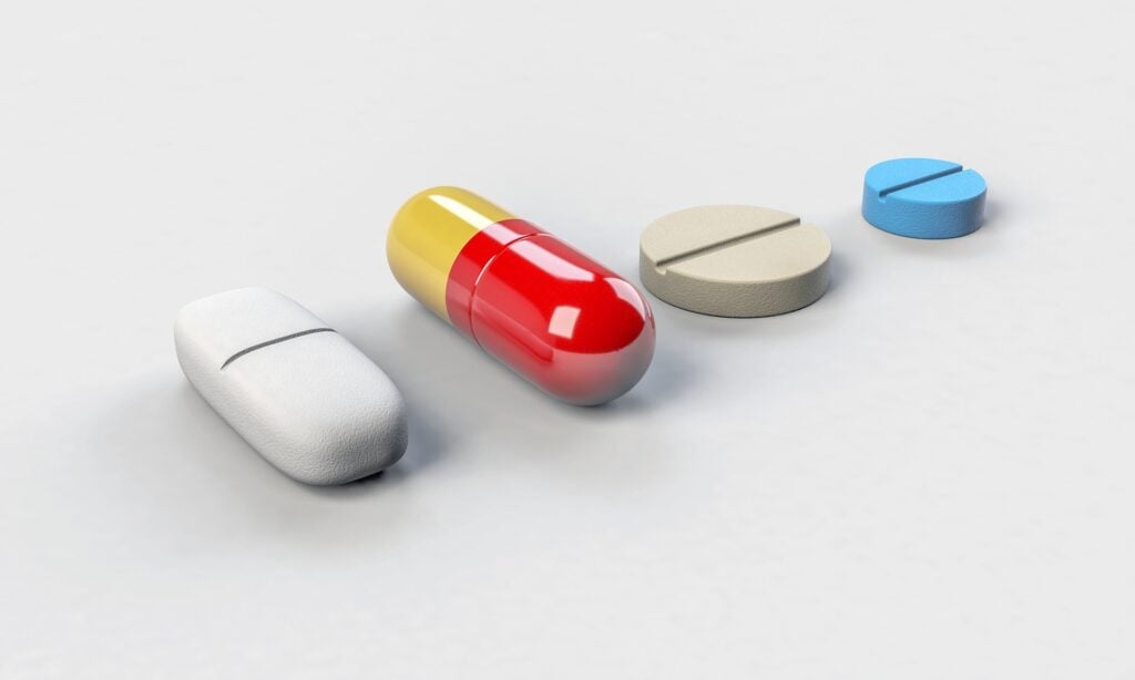 Three boring looking pills or vitamins with one bright red medicine capsule standing out in the row.