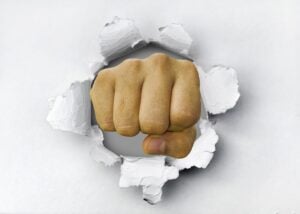 A fist punching through a white plaster wall, making impact.