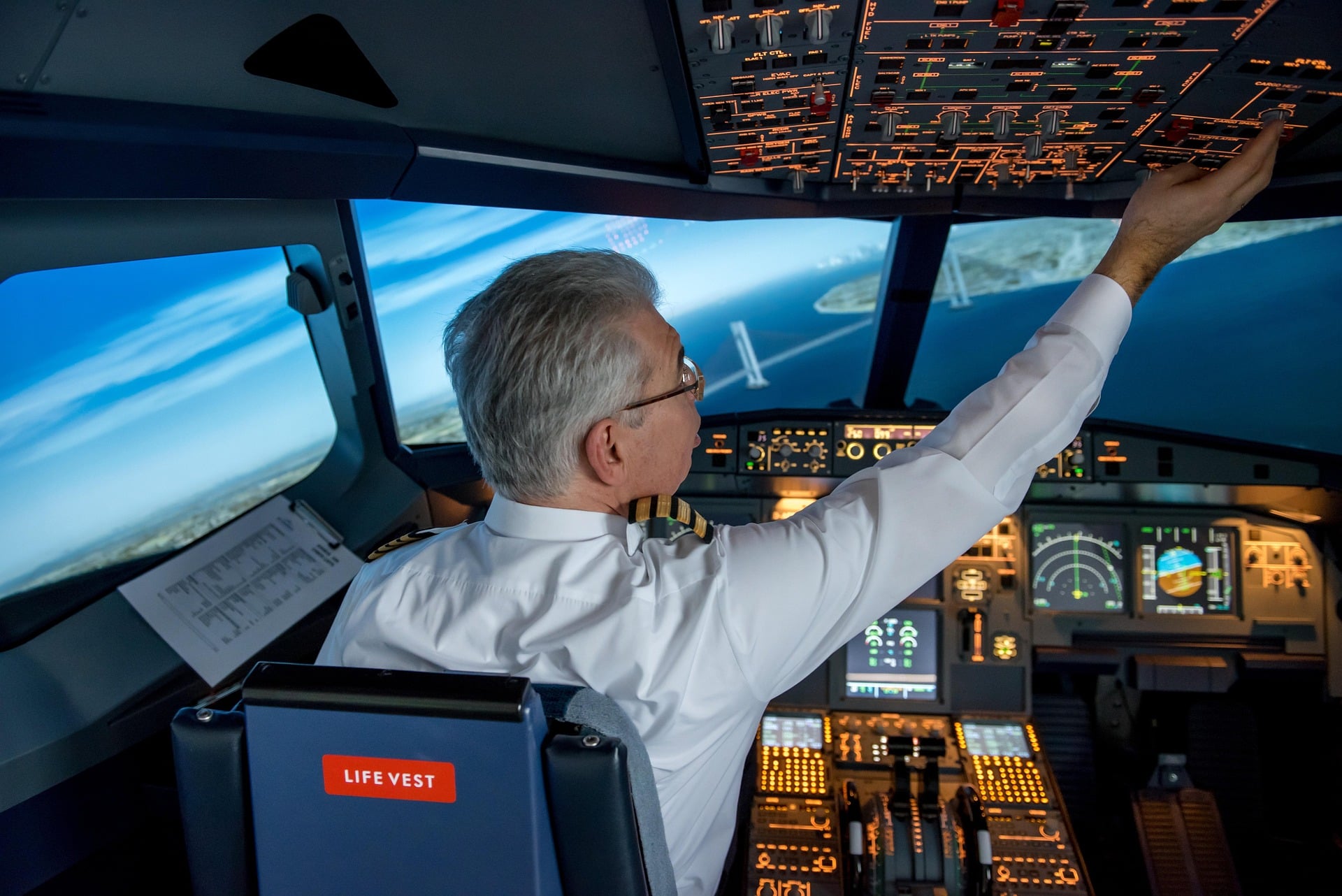 Pilot sitting in the cockpit of a jet, all the dashboard controls lit up, and skyline out the window.